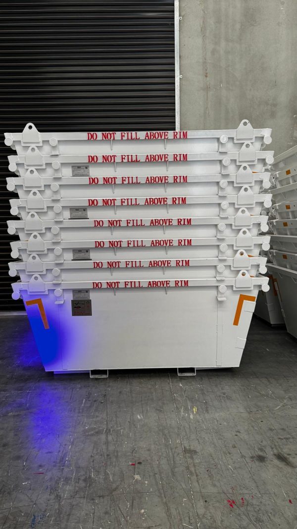 Stack of large white industrial crates with red 'DO NOT FILL ABOVE RIM' labels, stored against a concrete wall and metal shutter; blue/purple lighting at base.