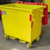 Yellow wheeled industrial waste bin with a red hinged lid in a warehouse setting.